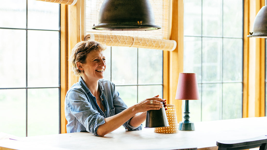 Our company's founder, Nicola Harding, seated at her desk with a warm smile, surrounded by our beautifully crafted lamps and lampshades, showcasing the passion and expertise behind our lighting products.