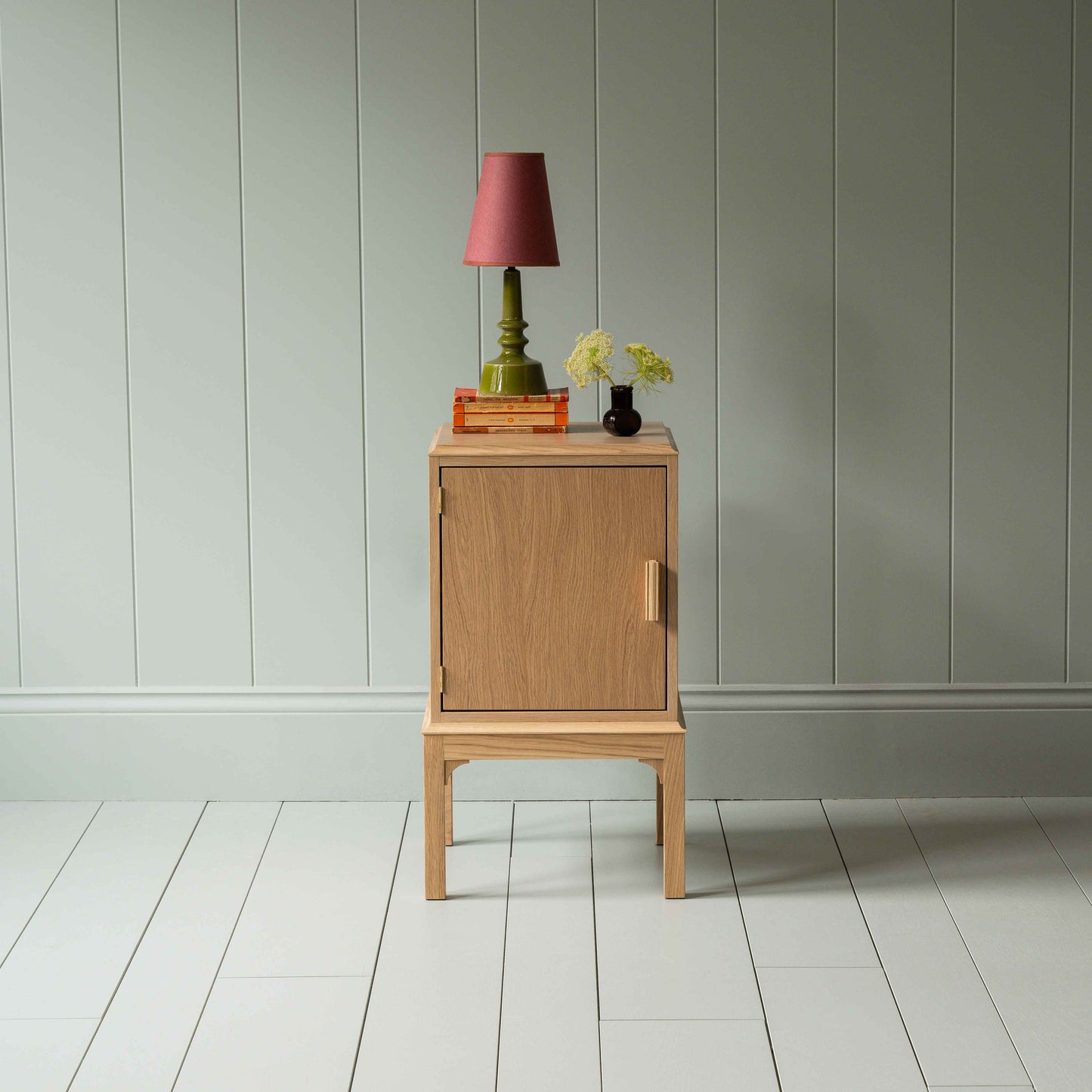 Bits and Bobs Bedside Table, Natural Oak, Left Hand Side Decorated with table lamp and a small bottle of flowers - Nicola Harding & Co.