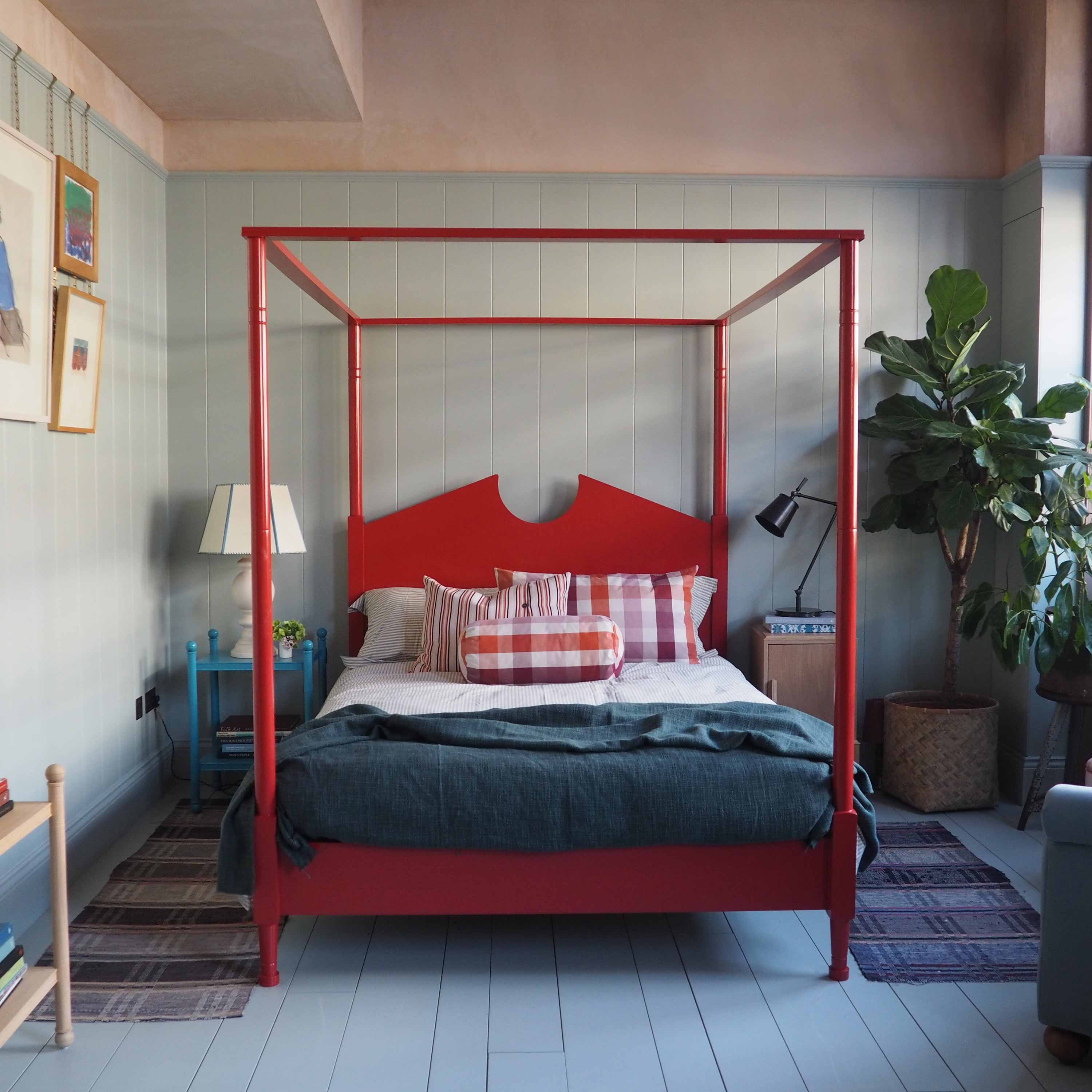 A red canopy bed in a bedroom with a lamp.