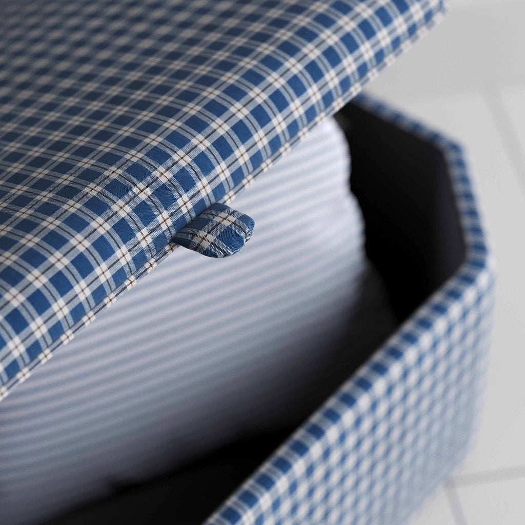 A close up of blue and white checkered ottoman on a wooden floor, providing a stylish and organized solution.