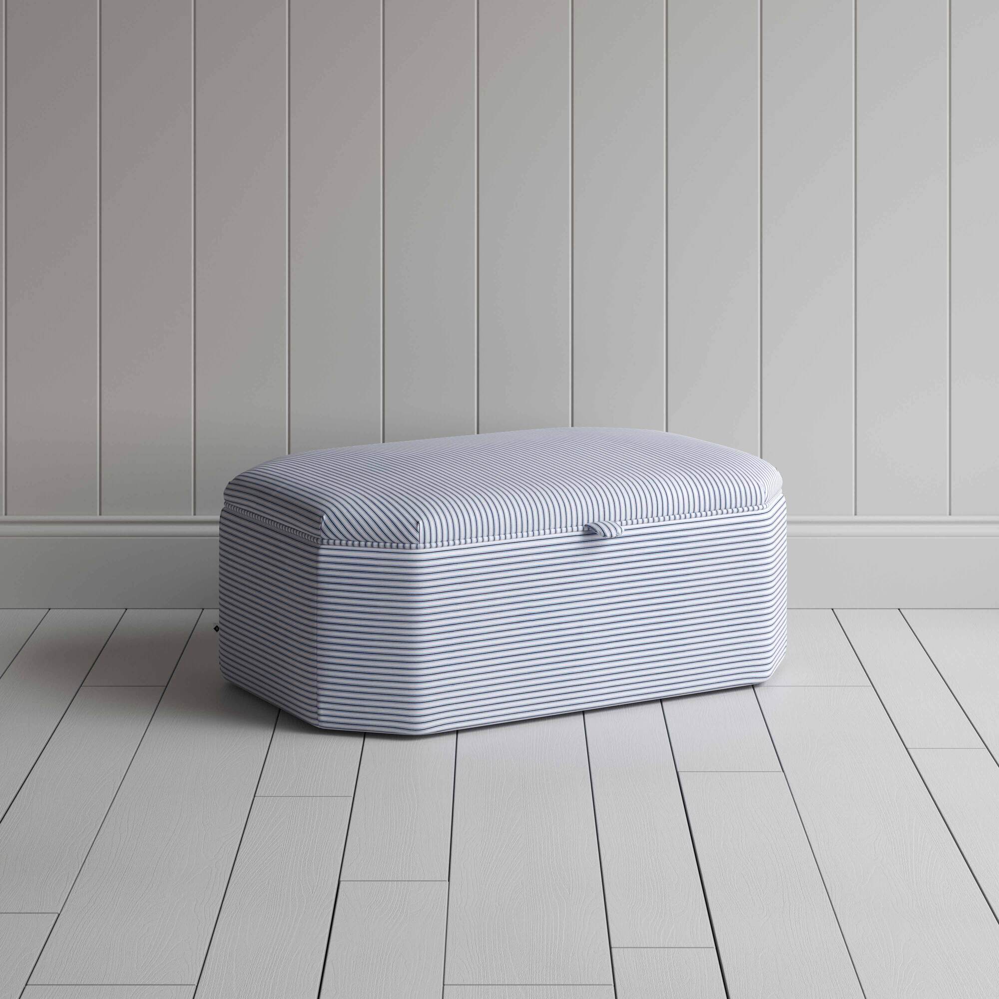A white and blue striped ottoman on a wooden floor, providing a stylish and practical storage solution.