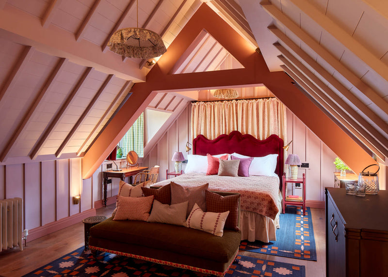 A cozy bedroom featuring a luxurious red velvet bed, complemented by warm lighting and an inviting ambiance. Beautifully designed by Nicola Harding and her team