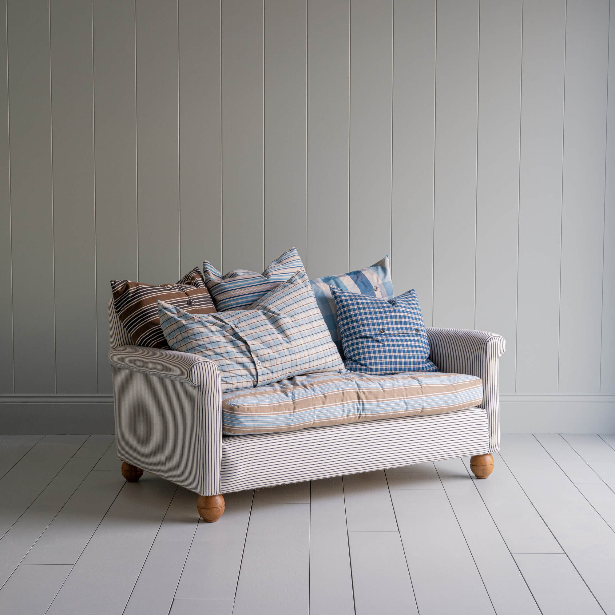 2-seater sofa in Ticking Cotton Chocolate Navy frame with a Regatta Blue seat, complemented by multiple NiX cushions - By Nicola Harding & Co
