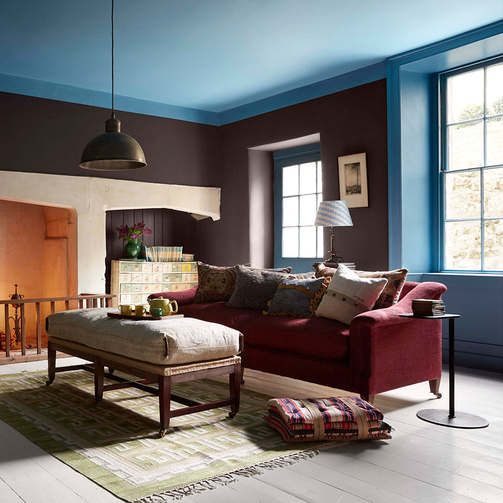 A cosy living room, meticulously crafted by Nicola Harding & Co, features a vibrant red sofa and a soothing blue ceiling.