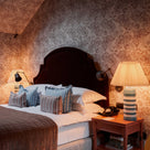 Bedroom decorated with Albion wallpaper in Mauve on the walls, featuring warm lighting and table lamps.