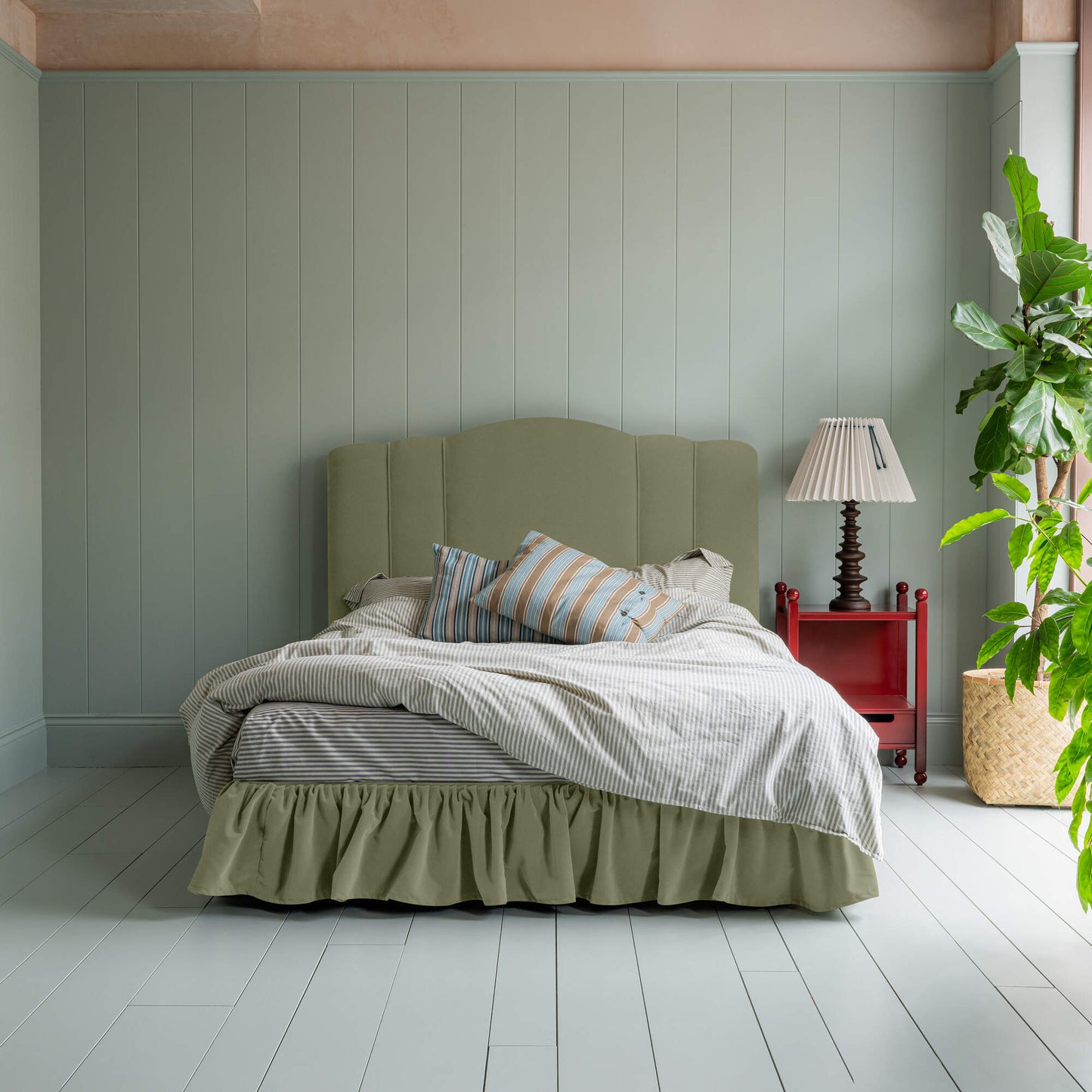 Cloud Nine Upholstered Bed in Intelligent Velvet Green Tea with Ruffled Valance, accompanied by a red side table with a lamp, pillows, and a blanket.