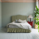 Cloud Nine Upholstered Bed in Intelligent Velvet Green Tea with Ruffled Valance, accompanied by a red side table with a lamp, pillows, and a blanket.