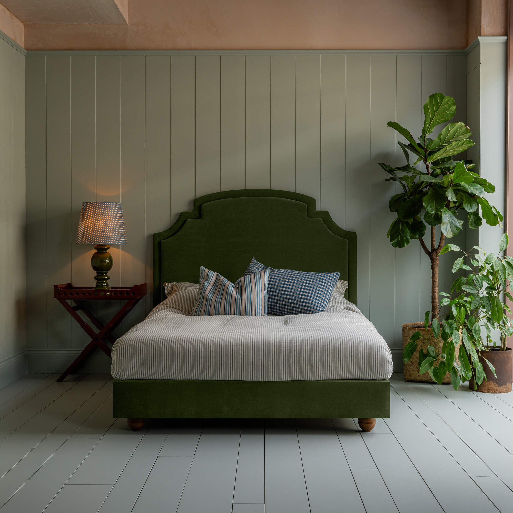 Seventh Heaven Upholstered Bed in Intelligent Velvet Juniper without Valance, accompanied by a side table lamp, pillows, and a blanket.