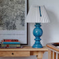 Sunburst Concertina Natural Pleat Lamp Shade with Peacock Blue Cord, With Hourglass Ceramic Table Lamp Base in Blue, On a Keepsake Console Table, Oiled Oak With Bunch of Books and a painting on the Wall - By NiX