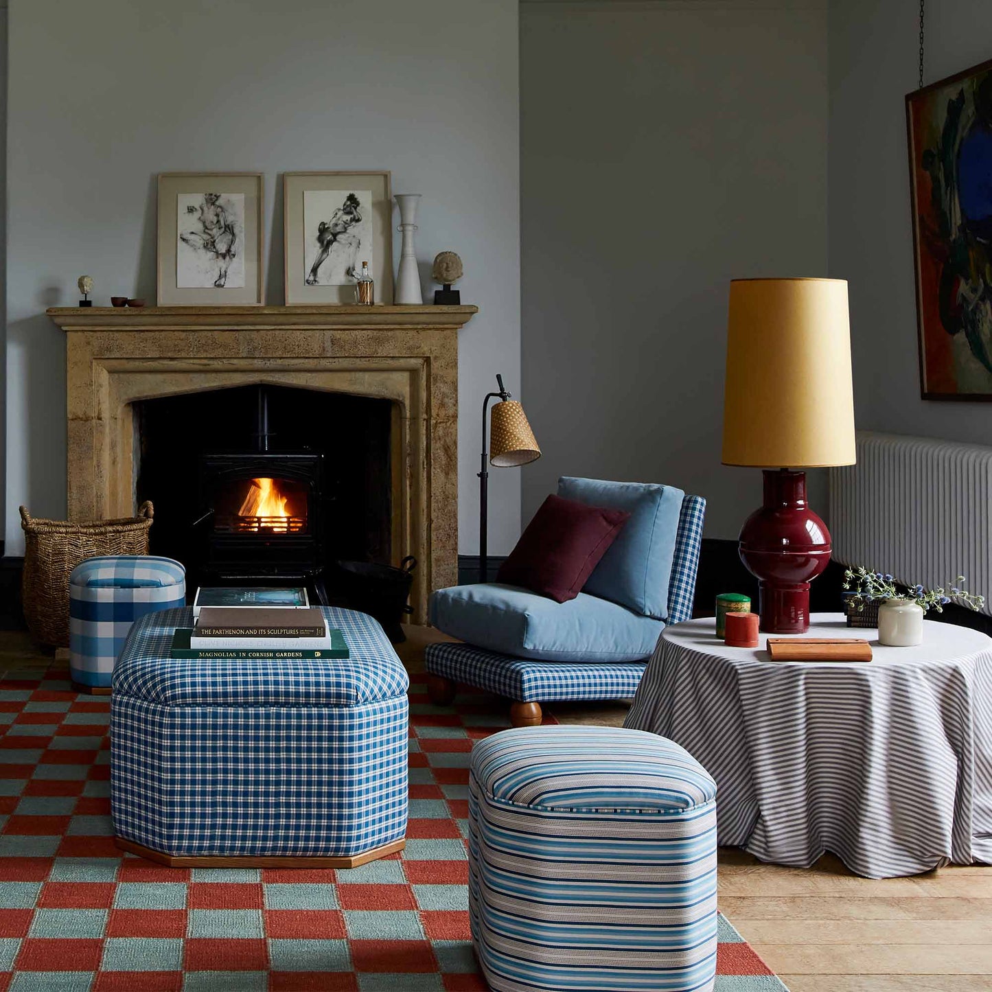 Orb Ceramic Table Lamp Base in Red, With Whimsical Tall Straight Empire Lamp Shade in Mustard with Antiqued Gold Trim, on a Side Table in the Living Room, With a Slipper Chair, 3 Ottomans Near a Fire Place - Nicola Harding