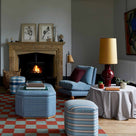 Orb Ceramic Table Lamp Base in Red, With Whimsical Tall Straight Empire Lamp Shade in Mustard with Antiqued Gold Trim, on a Side Table in the Living Room, With a Slipper Chair, 3 Ottomans Near a Fire Place - Nicola Harding