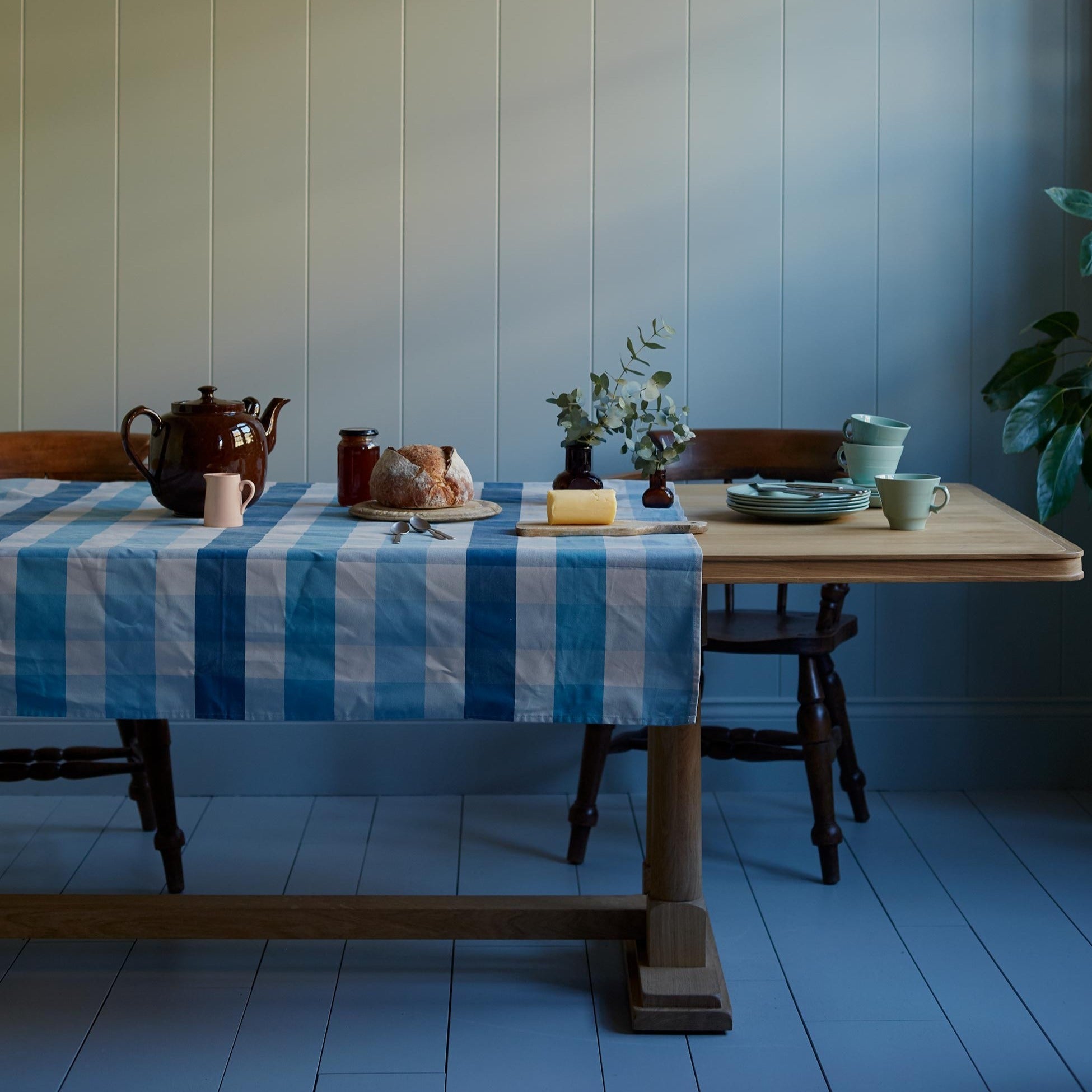 Tuck In rectangular dining table in oak, decorated with cotton fabric, set ready to serve tea with a teapot, cups, and pie, designed by Nicola Harding.