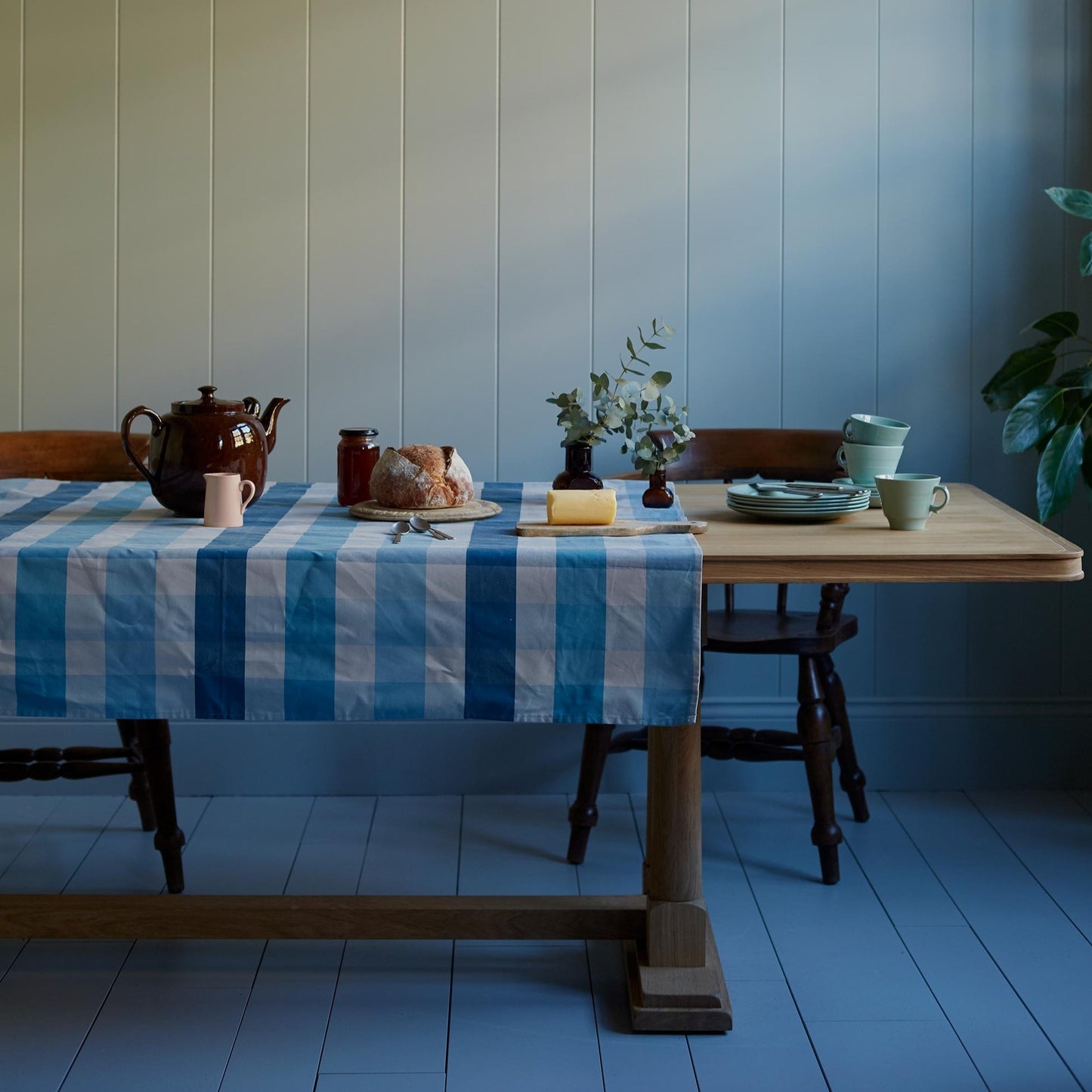 Tuck In rectangular dining table in oak, decorated with cotton fabric, set ready to serve tea with a teapot, cups, and pie, designed by Nicola Harding.