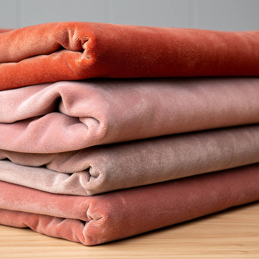 A stack of various shades of pink and red velvet fabrics folded neatly on top of each other