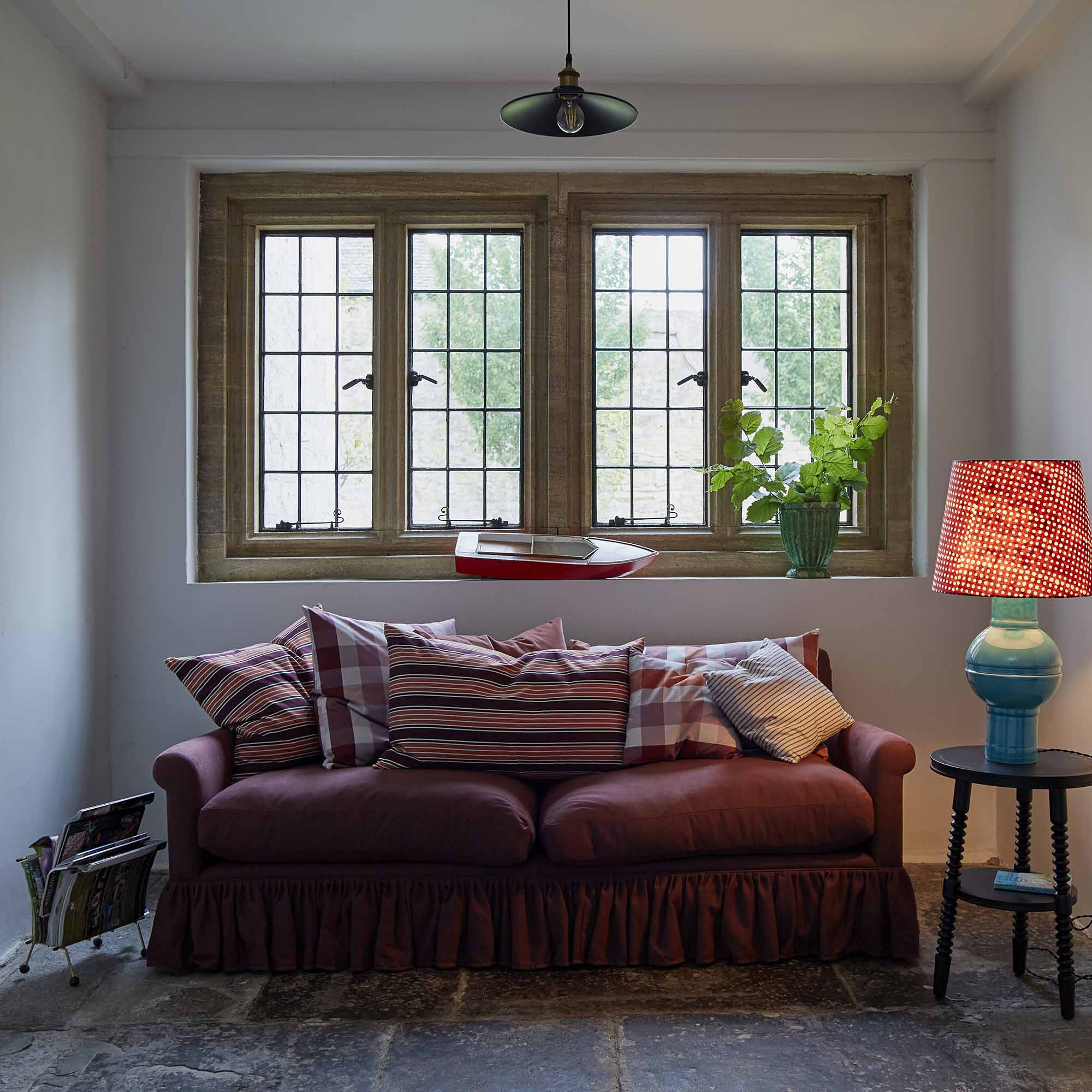  Elegant 4-seater sofa with decorative cushions placed near a window in a modern living room, accompanied by a side table and lamp. Designed by Nicola Harding & Co. 