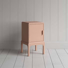 A small pink bedside table with a side door, perfect for storing items discreetly and adding a pop of color to any room. 