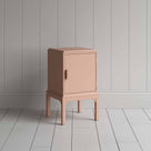  A small pink bedside table with a side door, perfect for storing items discreetly and adding a pop of color to any room. 