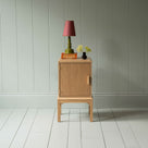  Bits and Bobs Bedside Table, Natural Oak, Left Hand Side Decorated with table lamp and a small bottle of flowers - Nicola Harding & Co. 