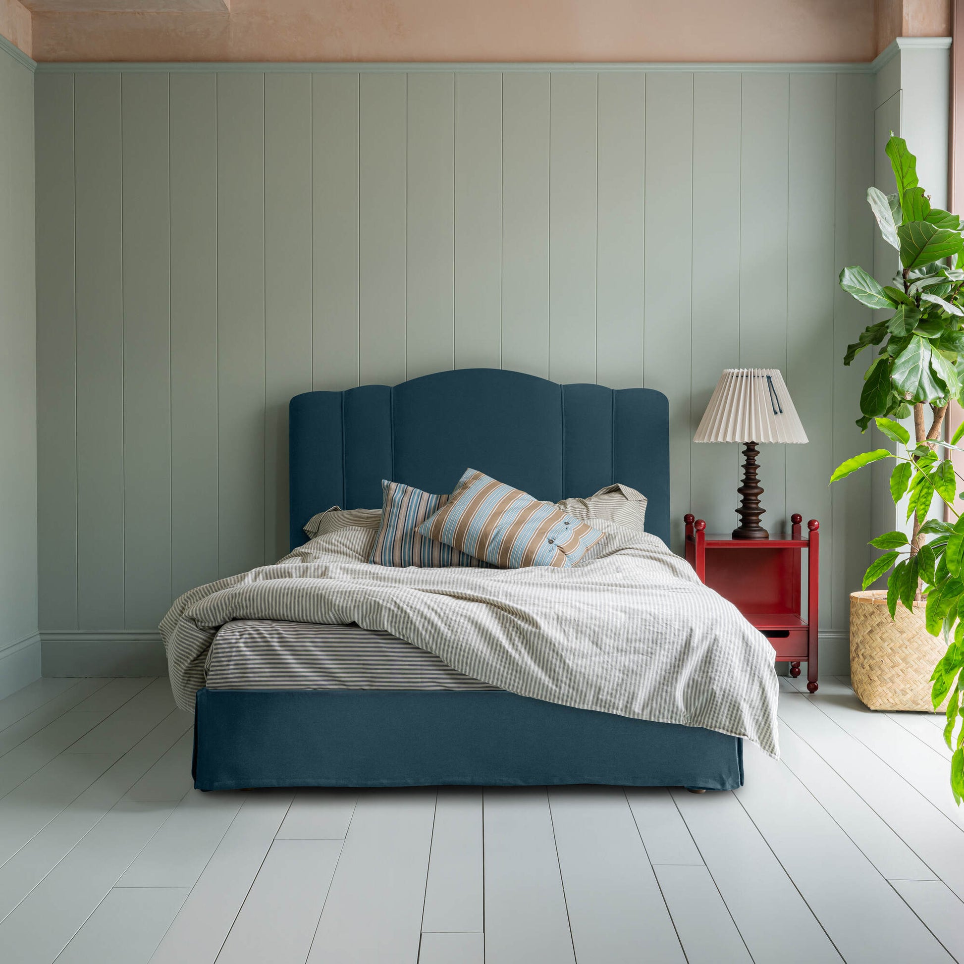 Cloud Nine Upholstered Bed in Intelligent Velvet Aegean with Ruffled Valance, accompanied by a red side table with lamp, pillows, and a blanket.