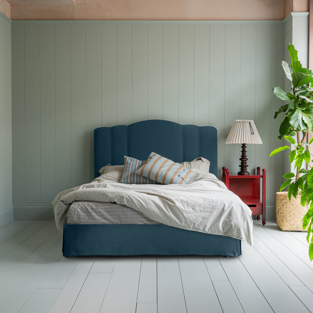  Cloud Nine Upholstered Bed in Intelligent Velvet Aegean with Ruffled Valance, accompanied by a red side table with lamp, pillows, and a blanket. 