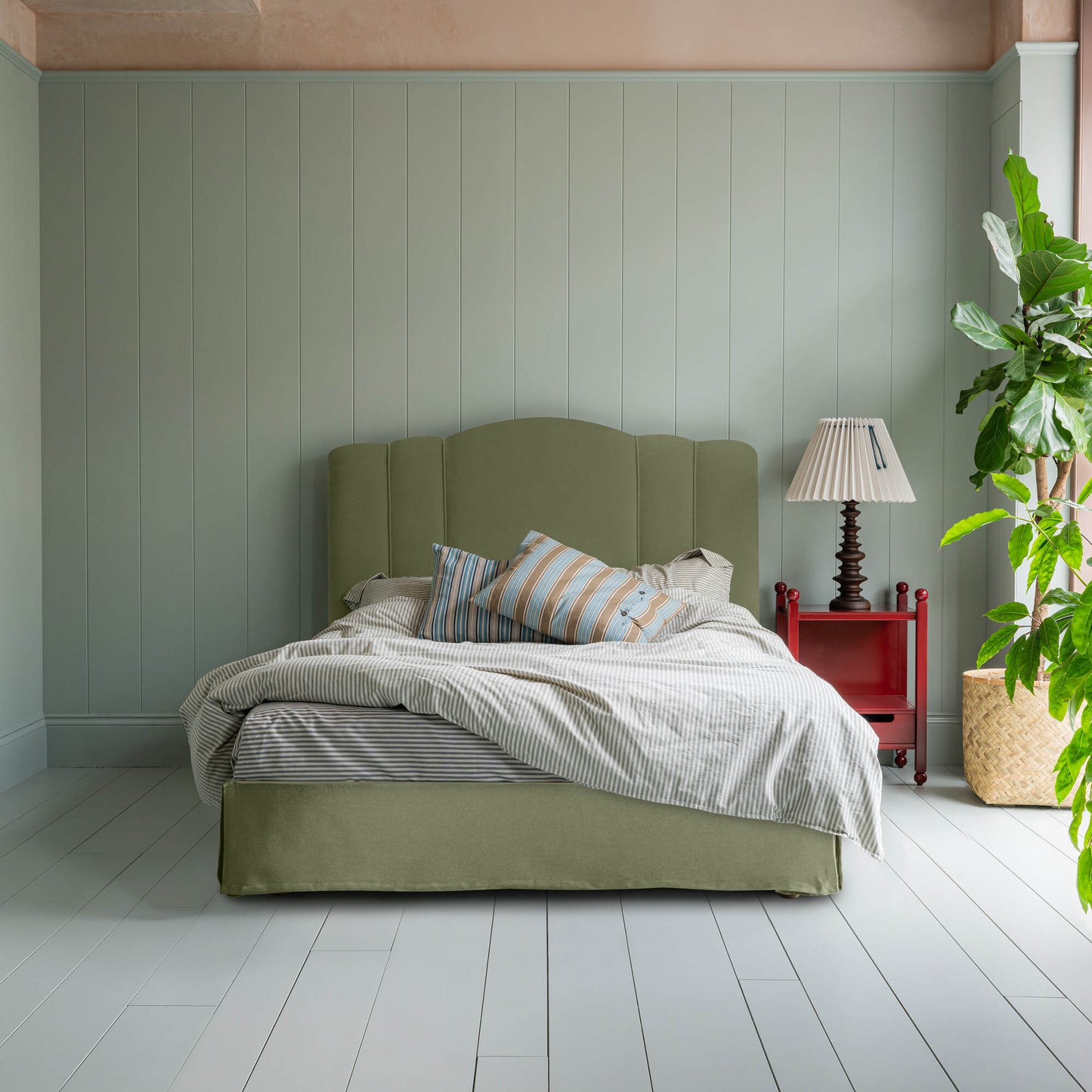 Cloud Nine Upholstered Bed in Intelligent Velvet Green Tea with Kick Pleat Valance, accompanied by a red side table with  lamp, pillows, and a blanket.