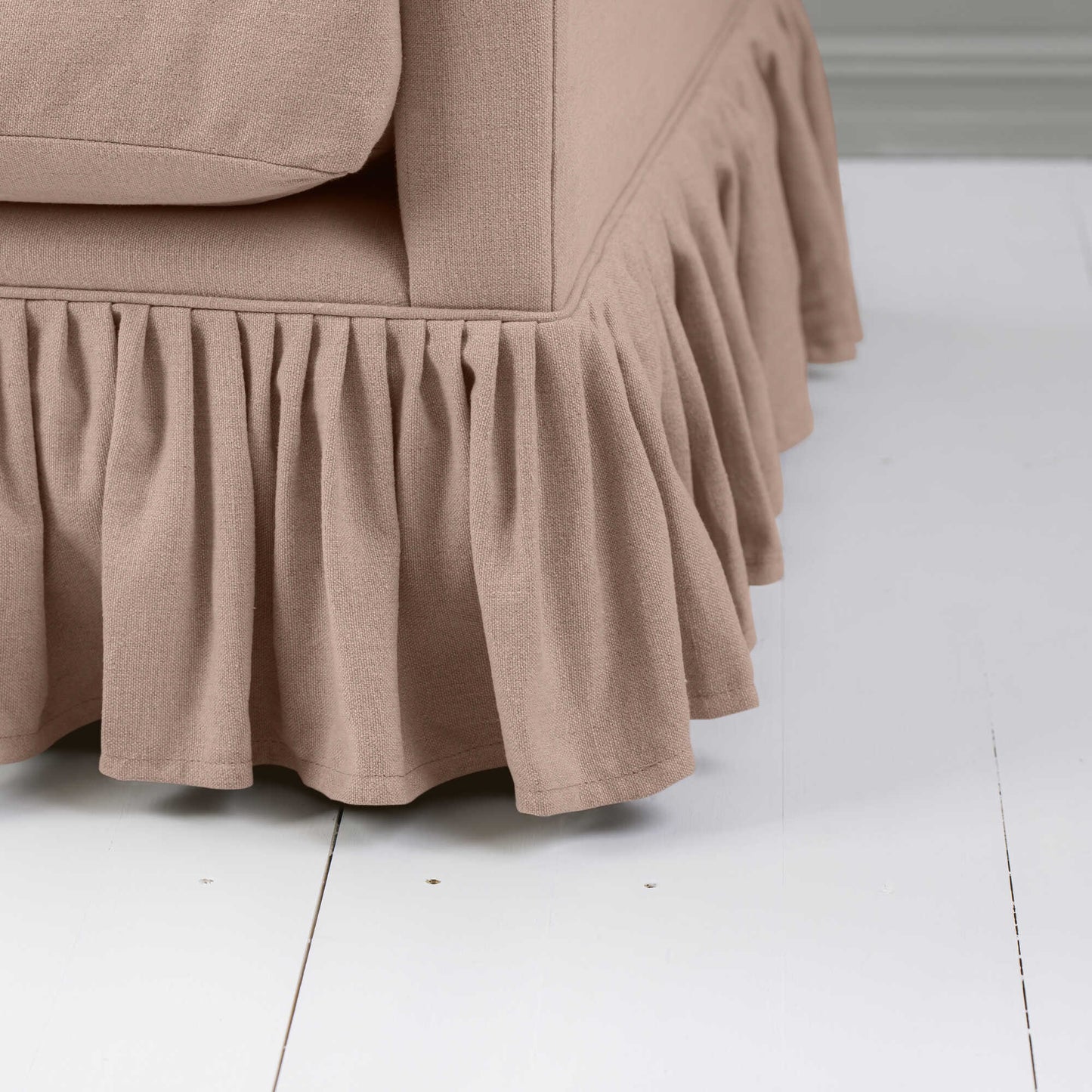 A close-up of a greyish orange couch with a ruffled skirt, adding elegance and charm to the overall aesthetic.