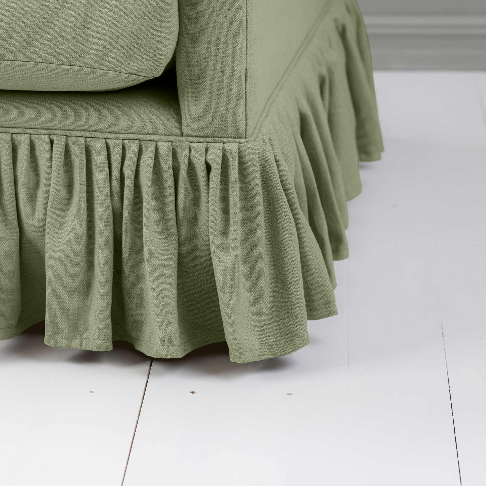  Close-up image of a green couch featuring a stylish ruffled skirt, enhancing the room's aesthetic. 