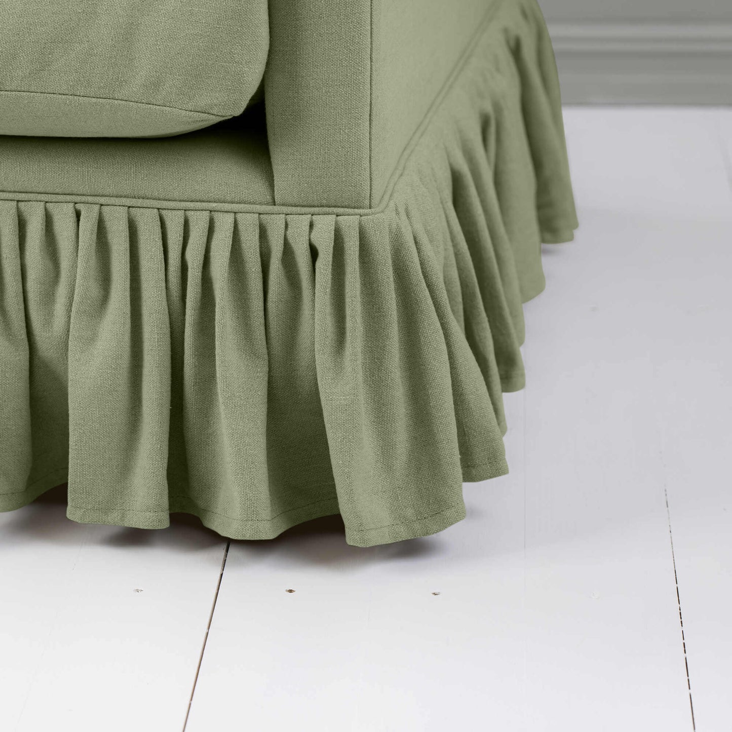 Close-up image of a green couch featuring a stylish ruffled skirt, enhancing the room's aesthetic.