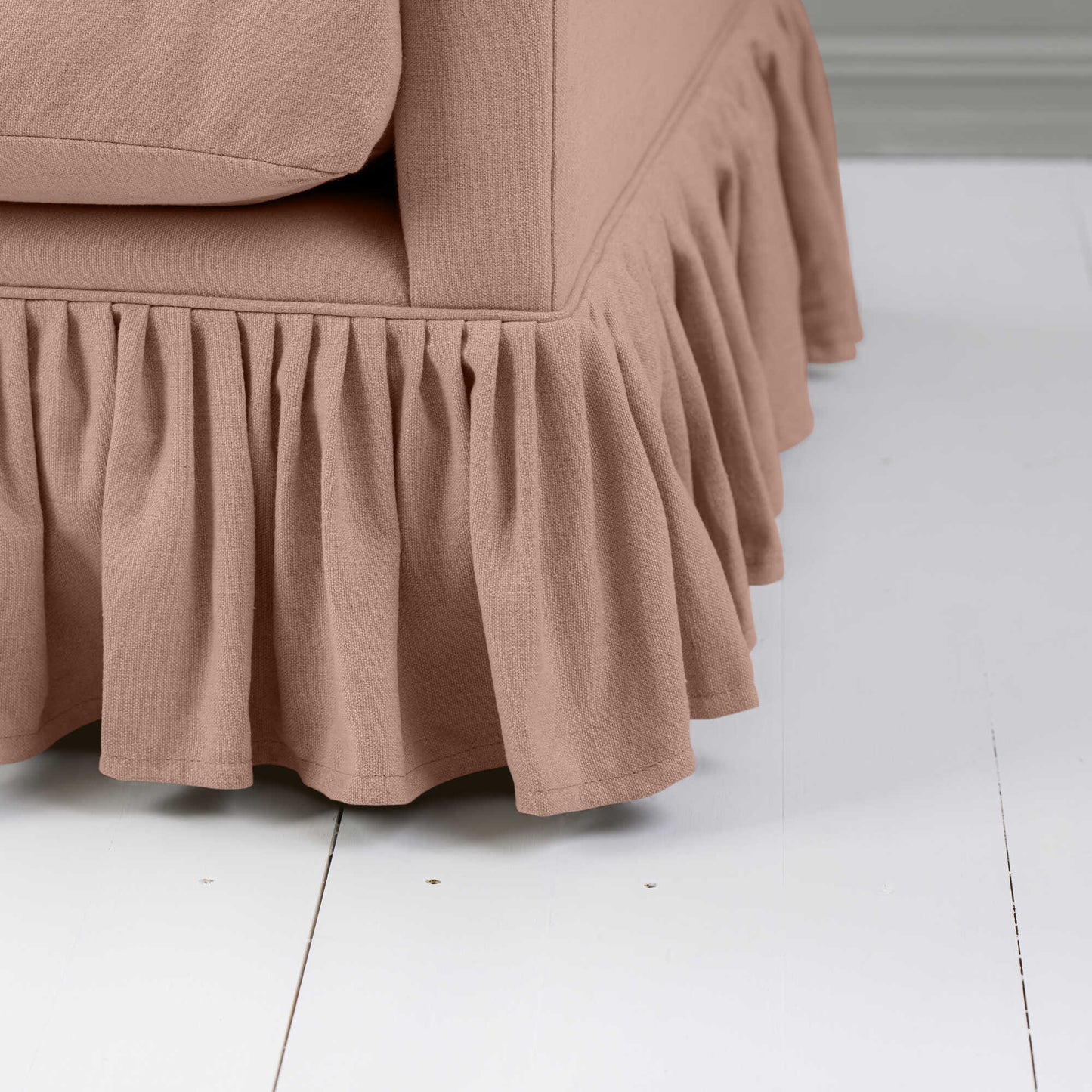 A detailed view of a pink sofa with a beautiful, ruffled skirt design for a cozy ambiance.