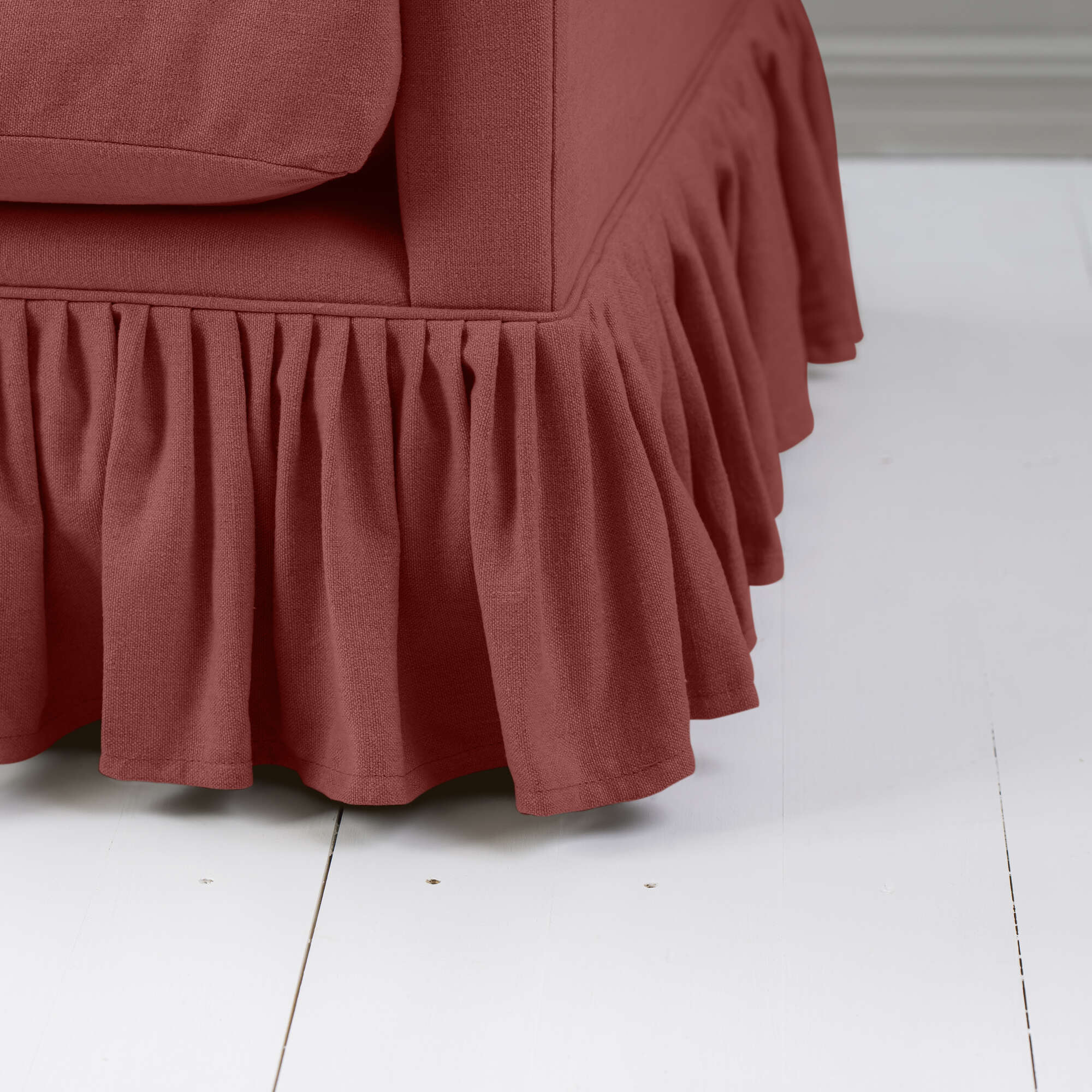  A detailed view of a red sofa with a beautiful, ruffled skirt design for a cozy ambiance. 