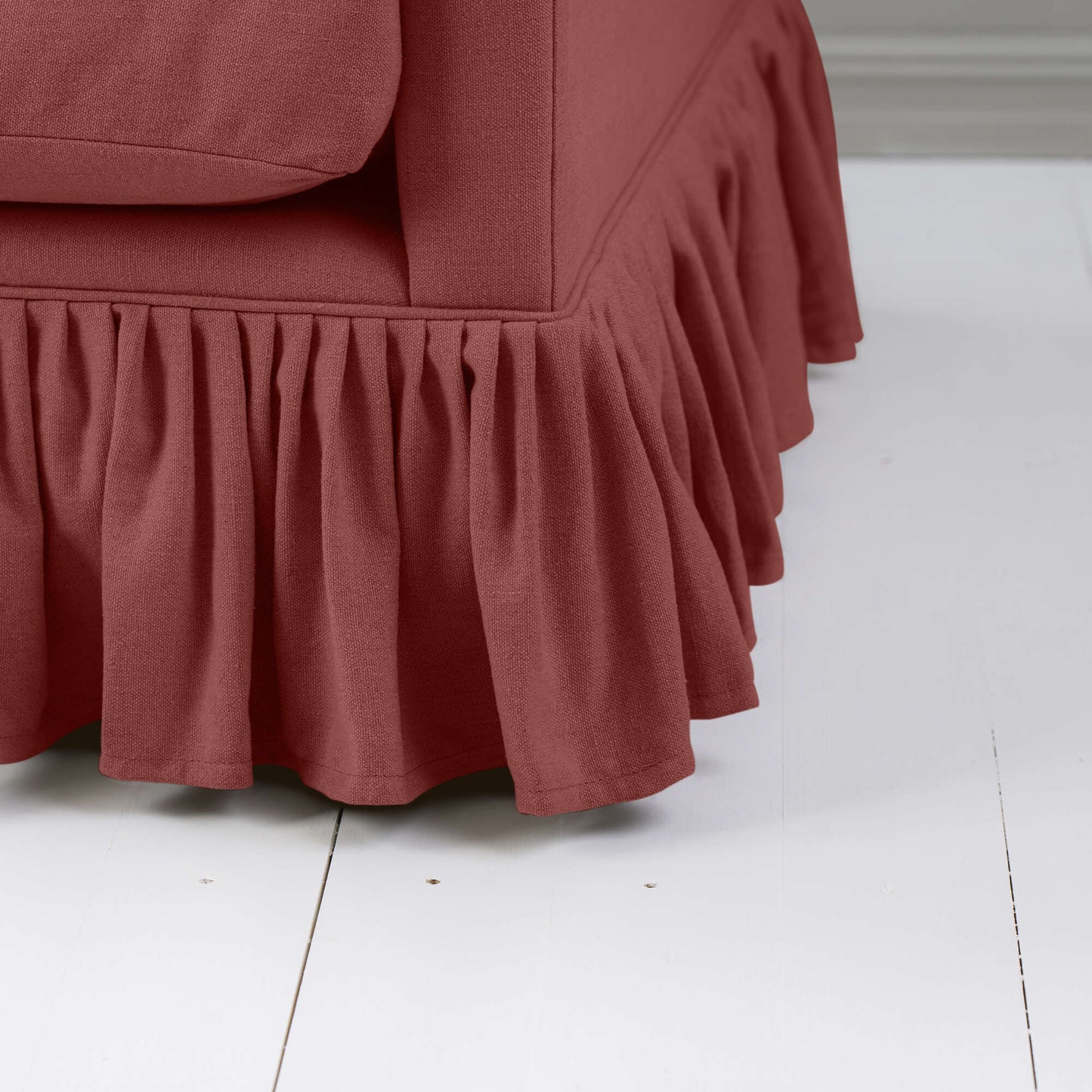 A detailed view of a red sofa with a beautiful, ruffled skirt design for a cozy ambiance.