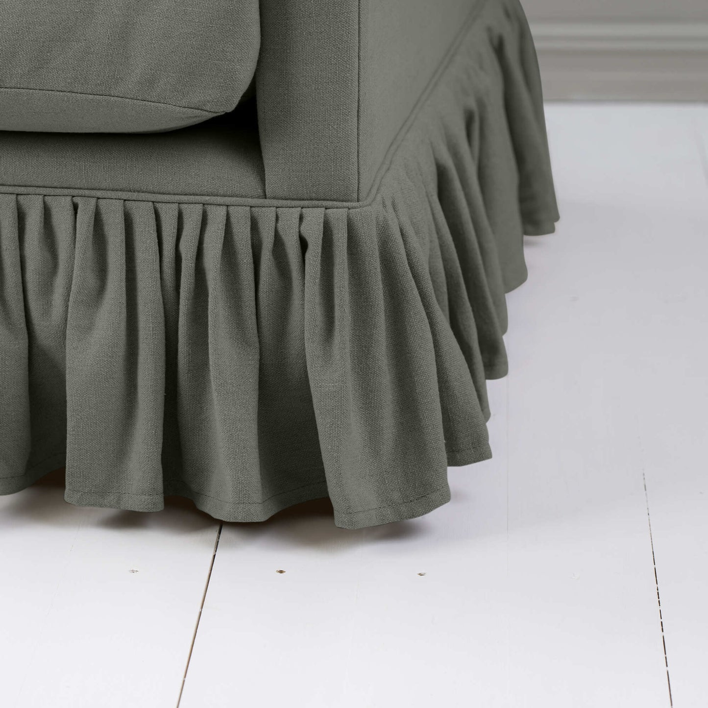 Close-up of a dark green couch with a ruffled skirt, adding a touch of elegance to the living room decor.