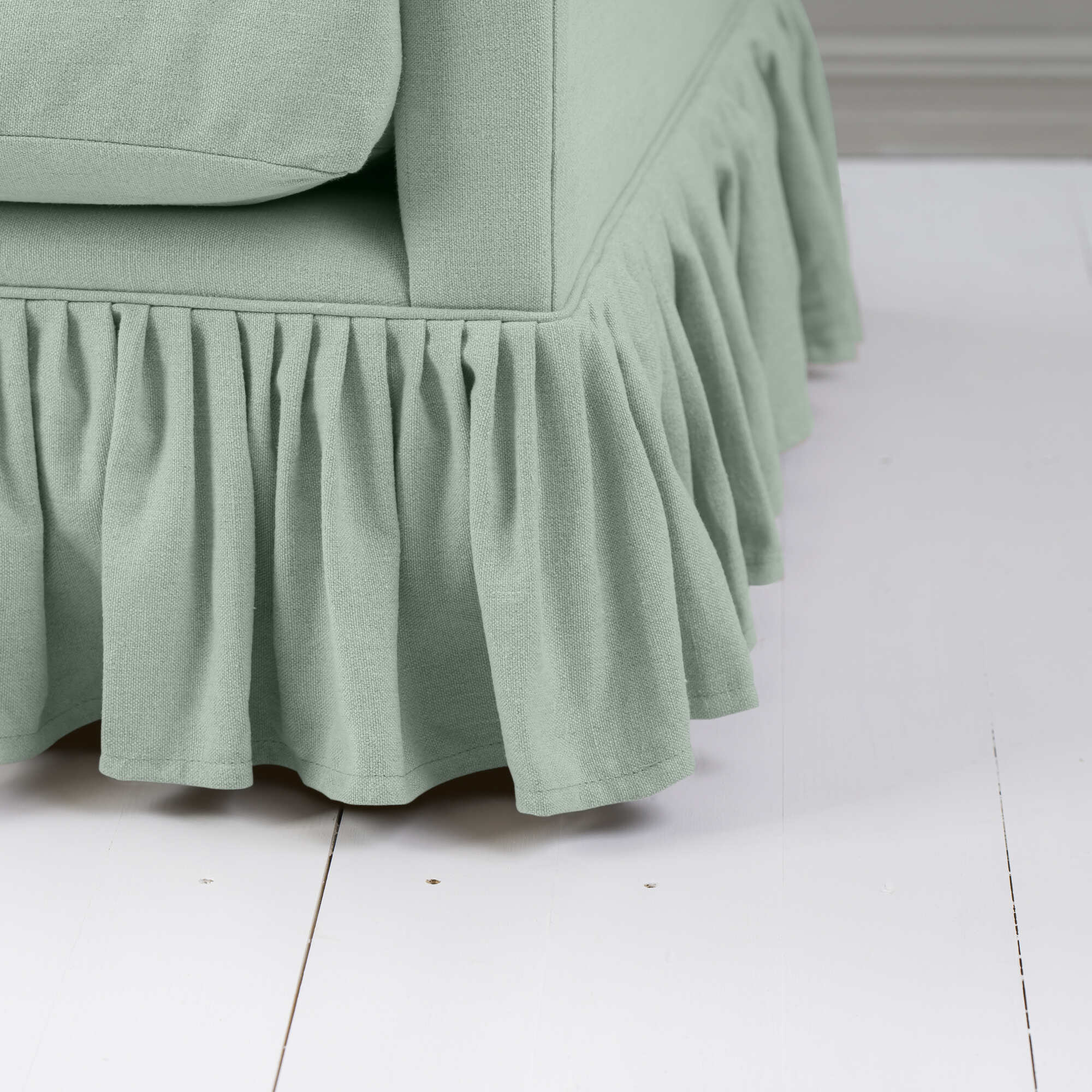  A close-up of a green couch with a ruffled skirt, adding charm to the room decor. 