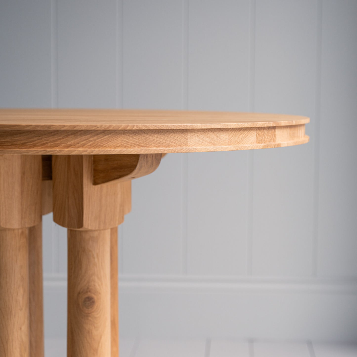 Edge design of the round lacquered oak wood dining table, showcasing its smooth finish from an eye-level front view.