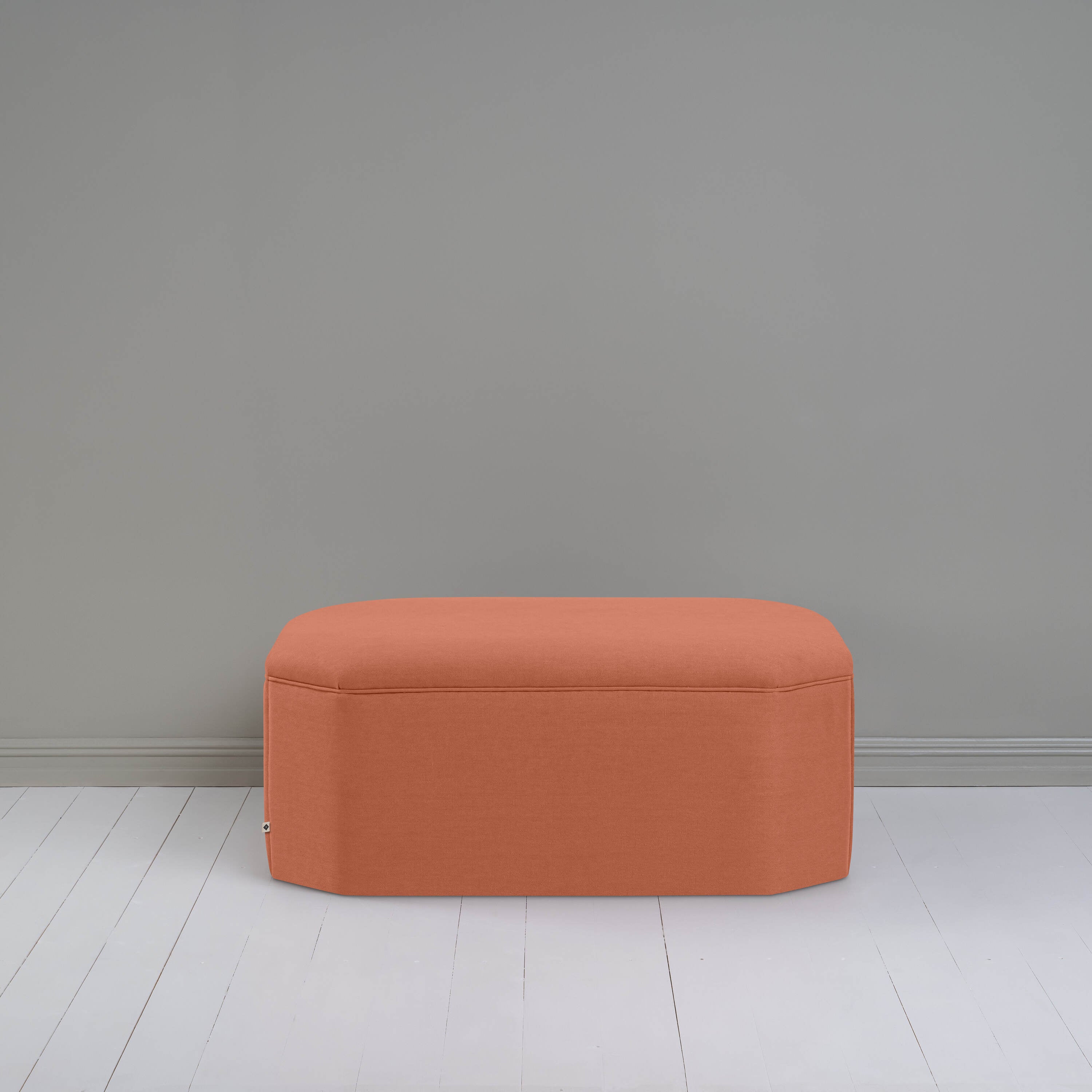  Small orange ottoman in room with gray wall, adding cozy touch to modern decor. 