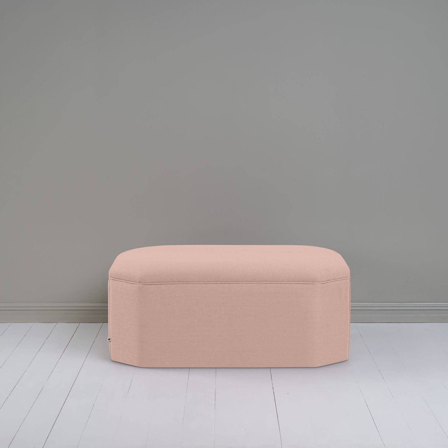 Light pink ottoman against gray wall in room.