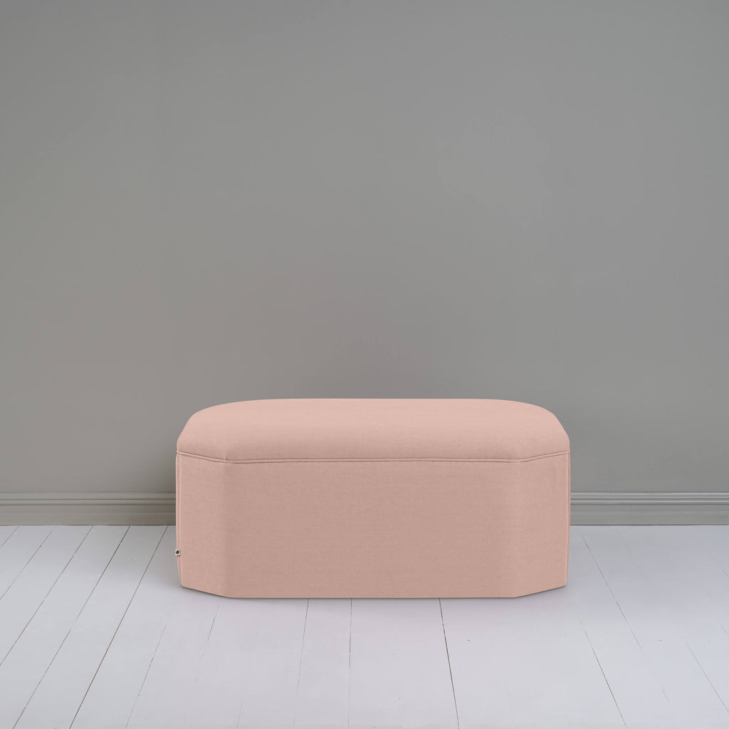  Light pink ottoman against gray wall in room. 