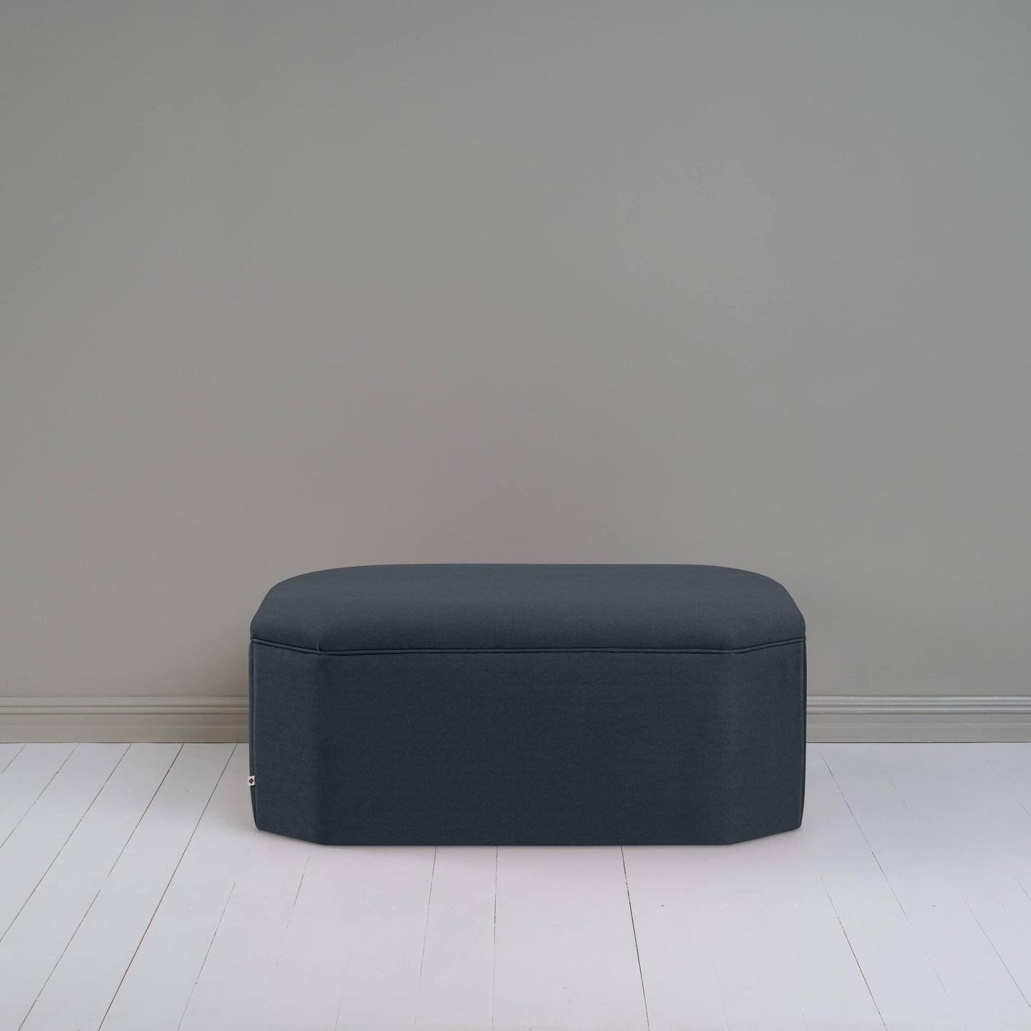 Black ottoman against gray wall in room.