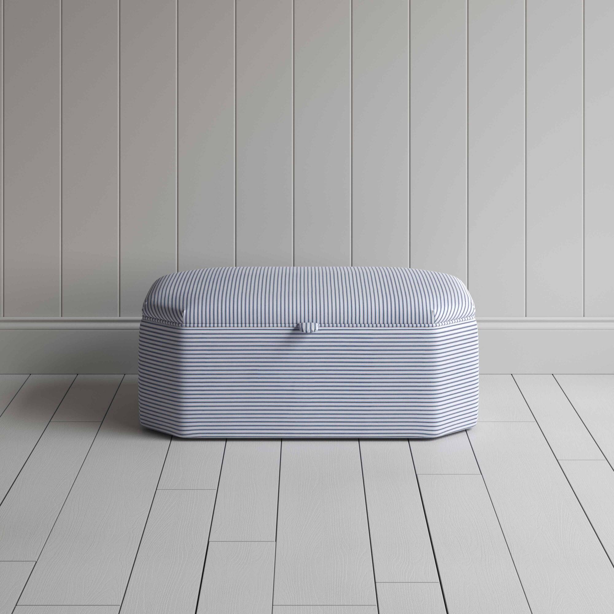  A white and blue striped ottoman on a wooden floor, providing a stylish and practical storage solution. 