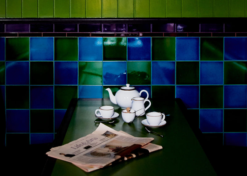 A table with a newspaper and a teapot on it.