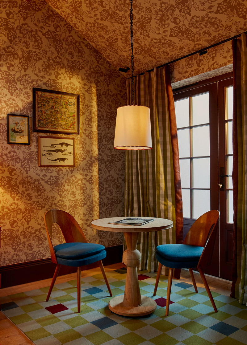 A room with a wooden table and two chairs, set against a patterned wall with a window on the side.