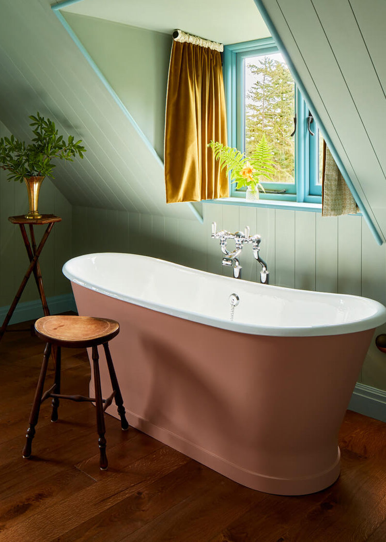 A bathroom with a white and pink tub and a wooden stool.