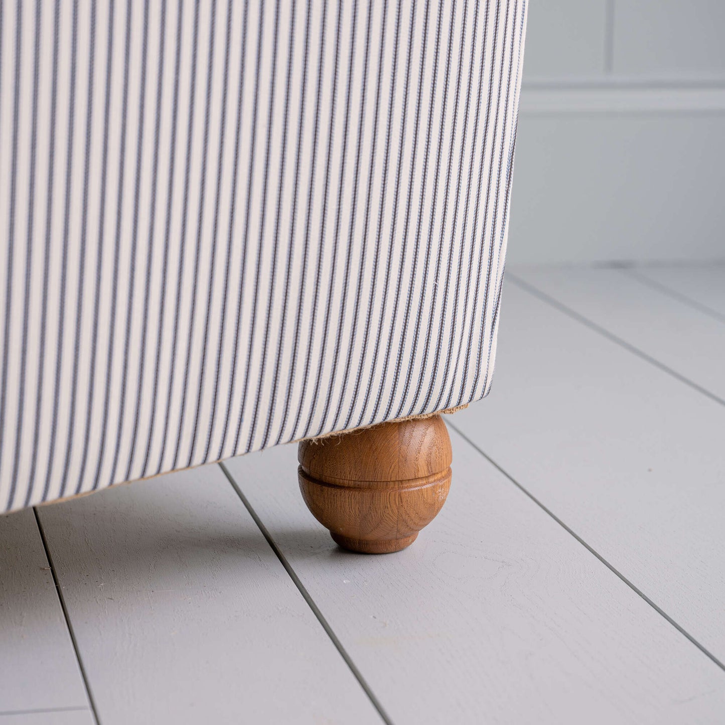 Close-up of the round wooden foot of the Idler 2-seater sofa in Ticking Cotton Chocolate Navy fabric, featuring a sturdy frame.