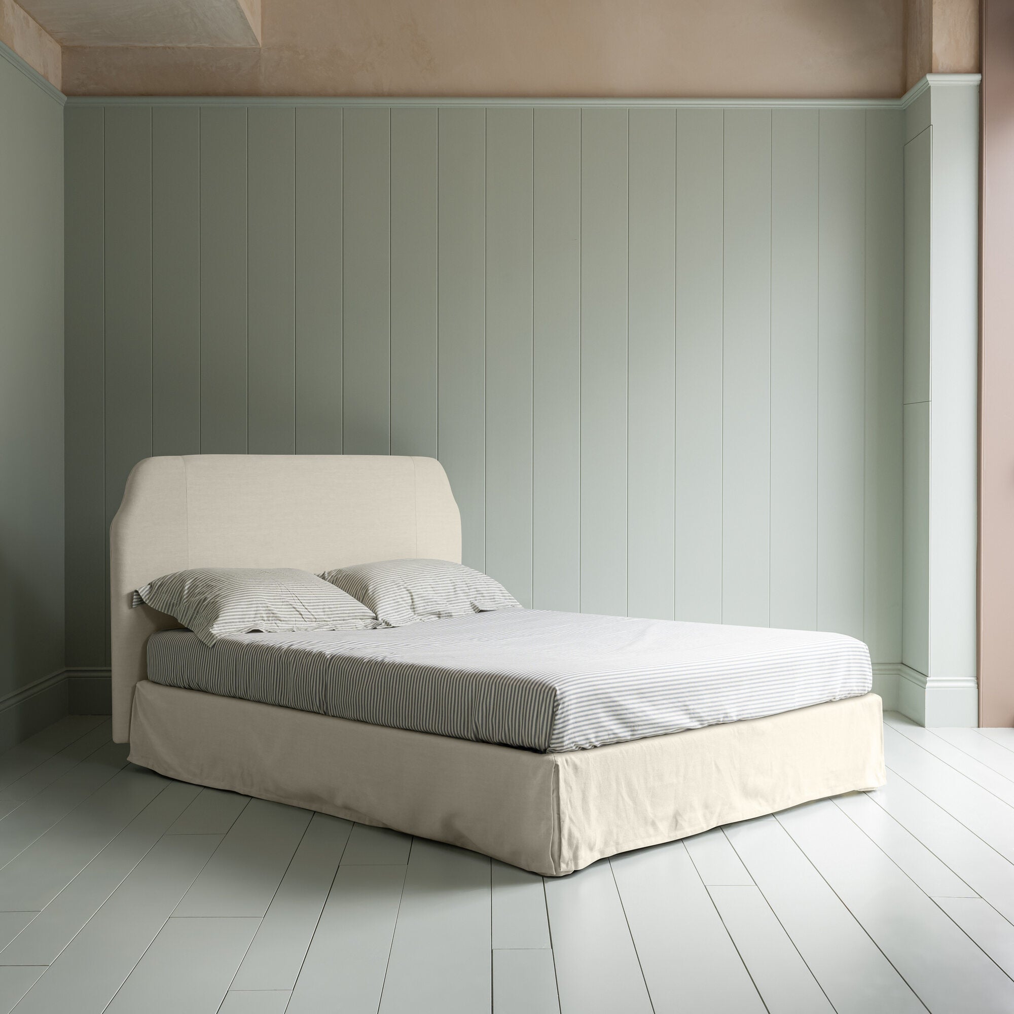  King-size upholstered bed by NiX in laidback linen dove with a kick pleat valance, shown in a complete side view. 