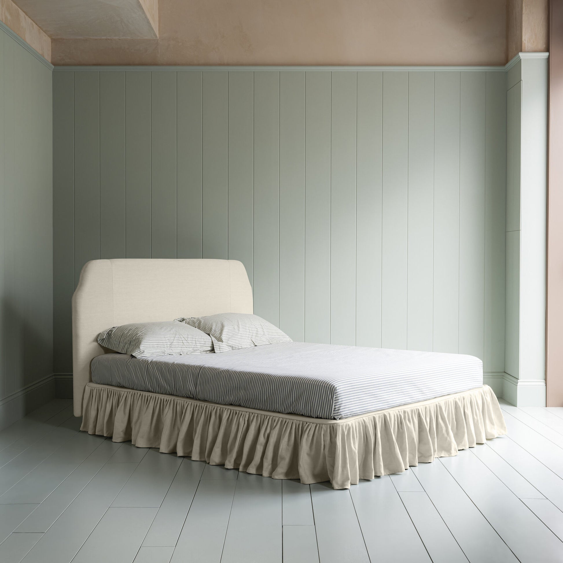 King-size upholstered bed in laidback linen dove with a ruffled valance, showing a complete side view with mattress and pillows.