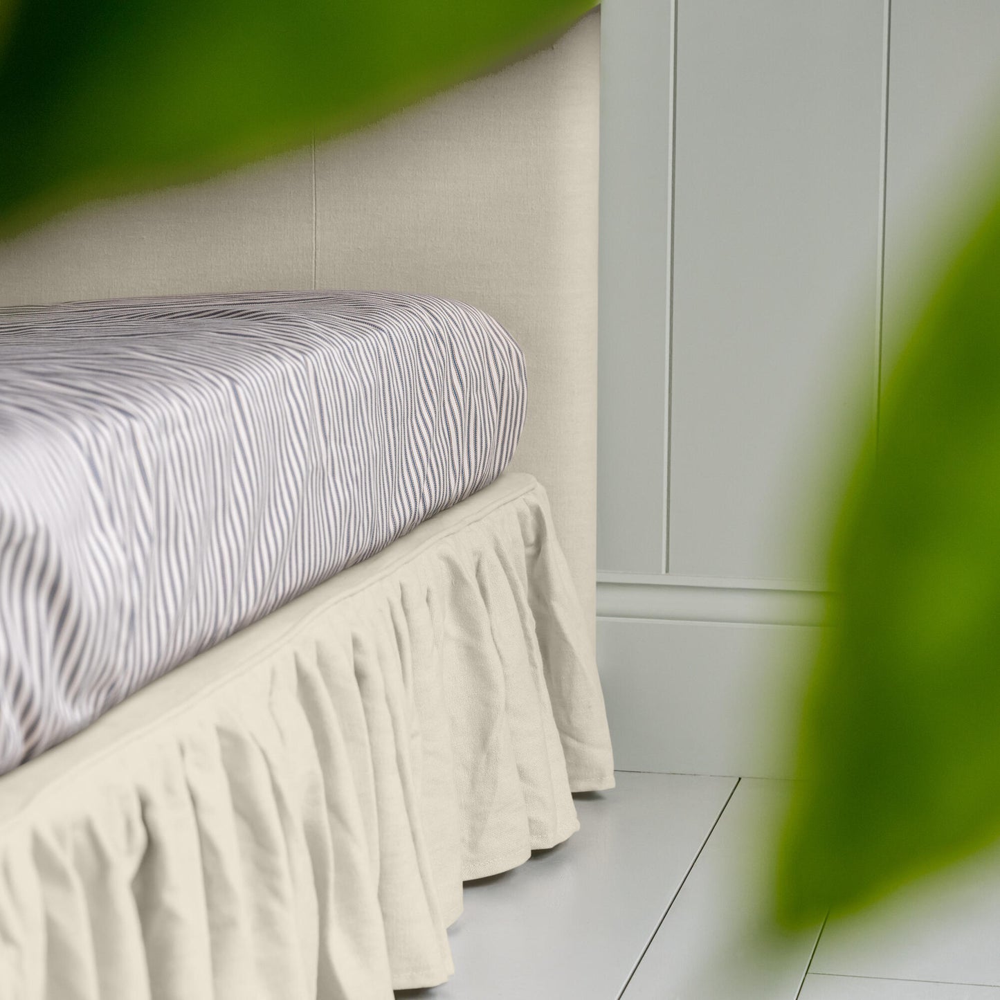 Upholstered Bed in Laidback Linen Dove with a ruffled valance, highlighting the side design and neatly tucked-in bedsheet.