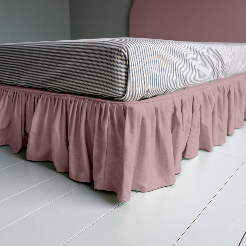  Upholstered bed in laidback linen heather with a ruffled valance, showcasing the edge design and a neatly tucked-in bedsheet. 