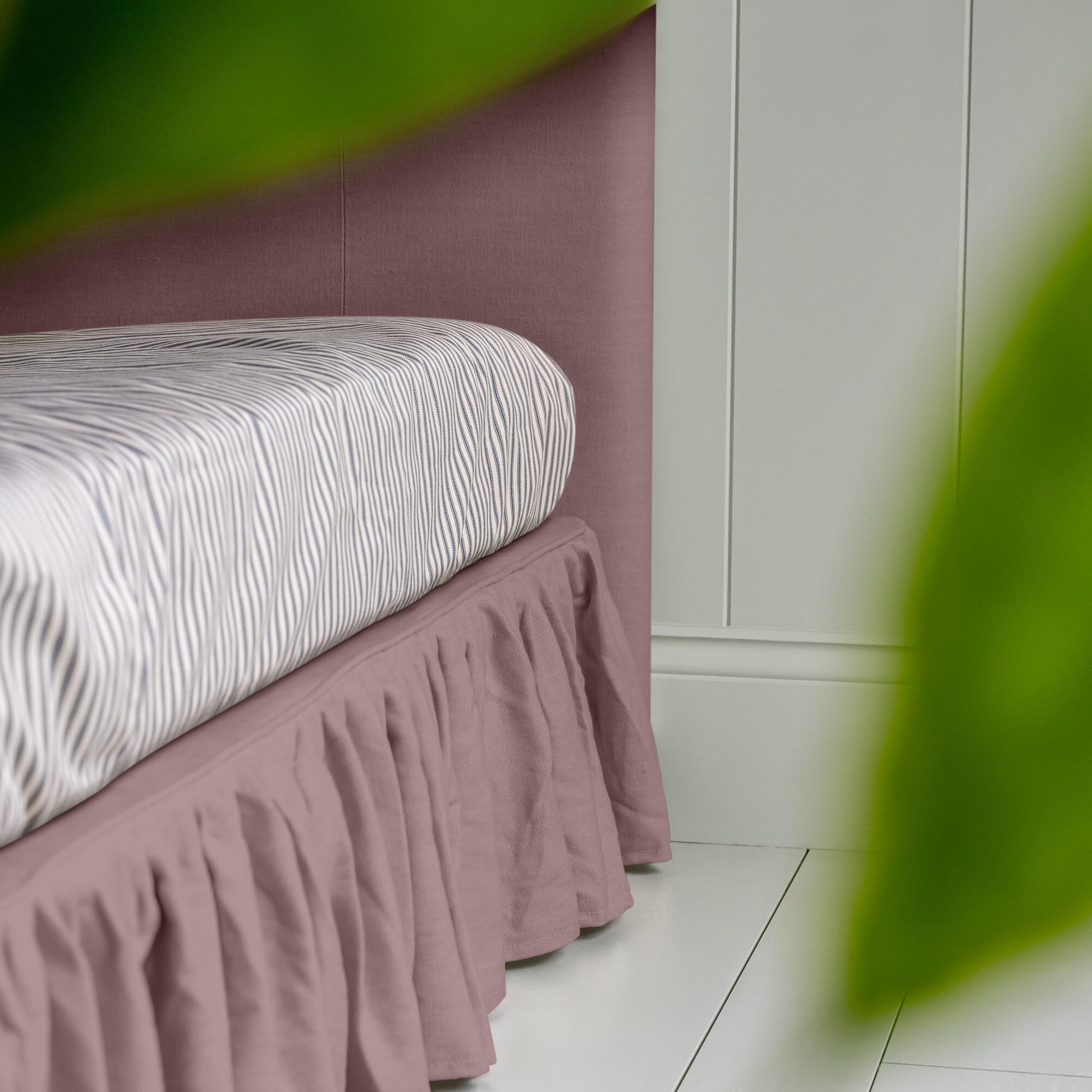 Upholstered bed in laidback linen heather with a ruffled valance, highlighting the side design and neatly tucked-in bedsheet.