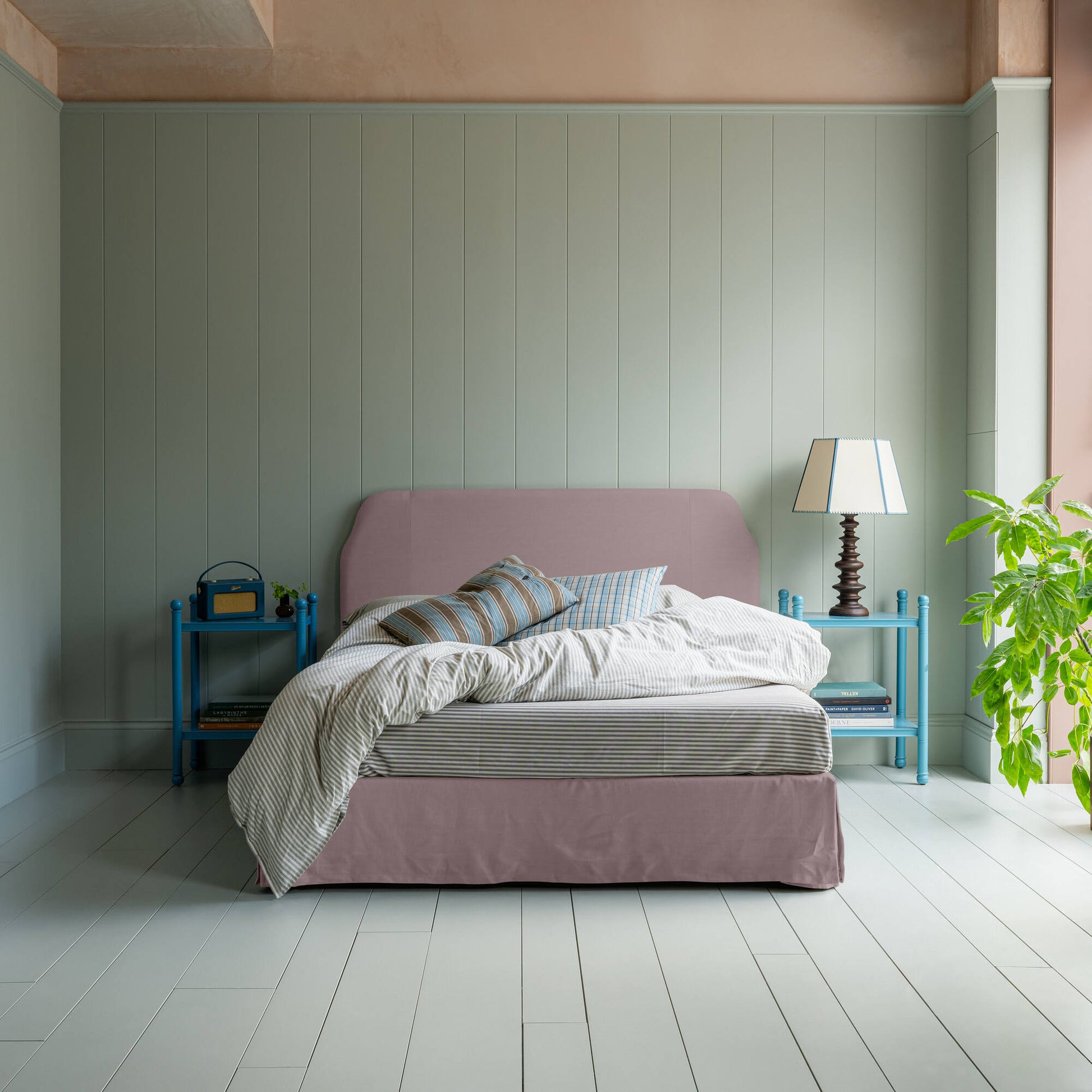 Dream Ticket Upholstered Bed in Laidback Linen Heather with Kick Pleat Valance, accompanied by pillows, and a blanket with 2 side tables one have a lamp.