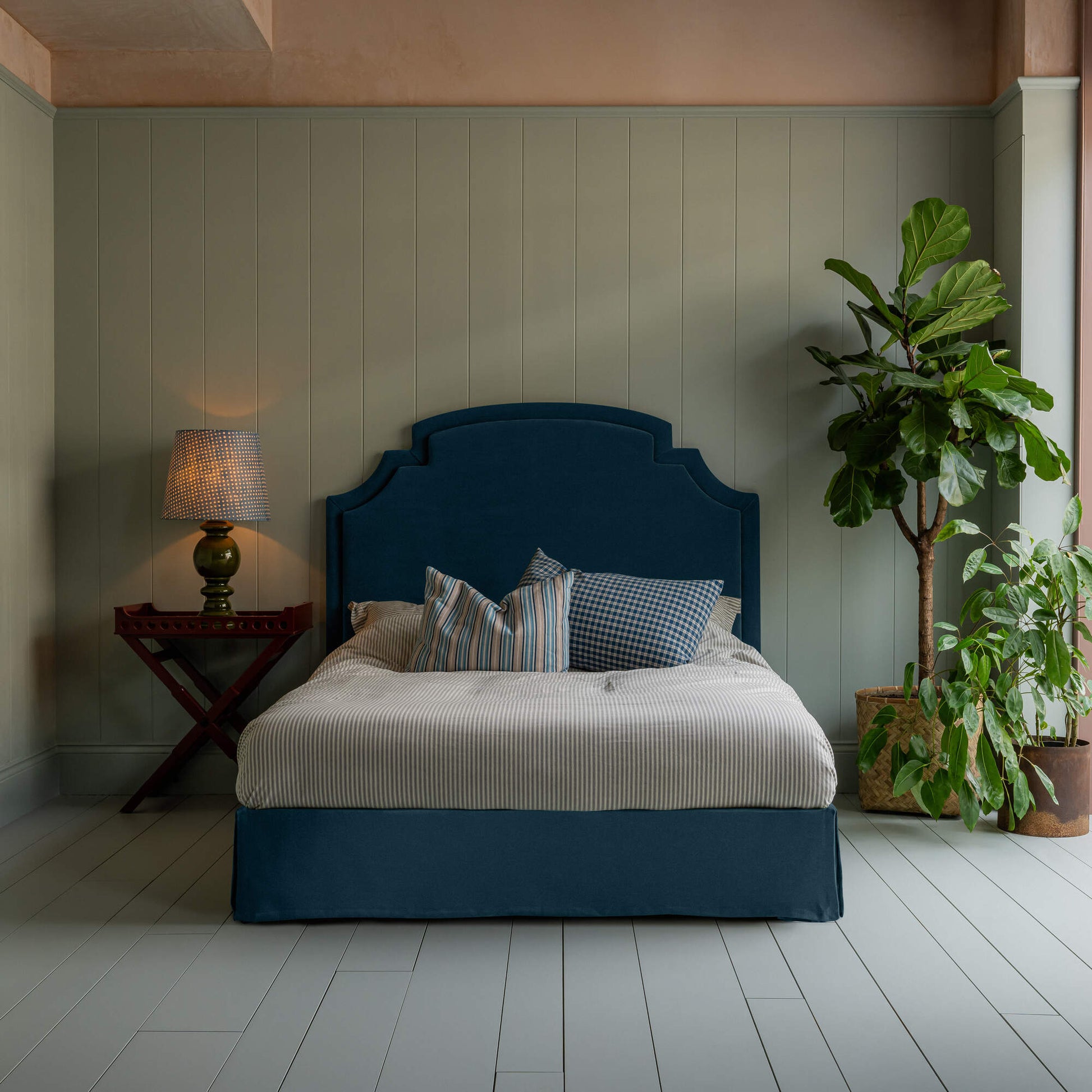 Seventh Heaven Upholstered Bed in Intelligent Velvet Aegean with Kick Pleat Valance, accompanied by a side table lamp, pillows, and a blanket.